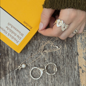 Sisyphus Necklace laying on a wooden table with other jewelry